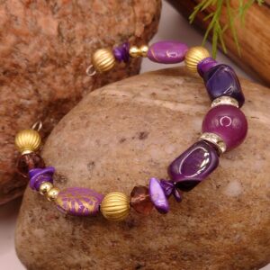 Fioletowa bransoletka na drucie pamięciowym z centralnym koralikiem, złotymi przekładkami z kryształkami oraz muszlowymi kamyczkami, biżuteria handmade