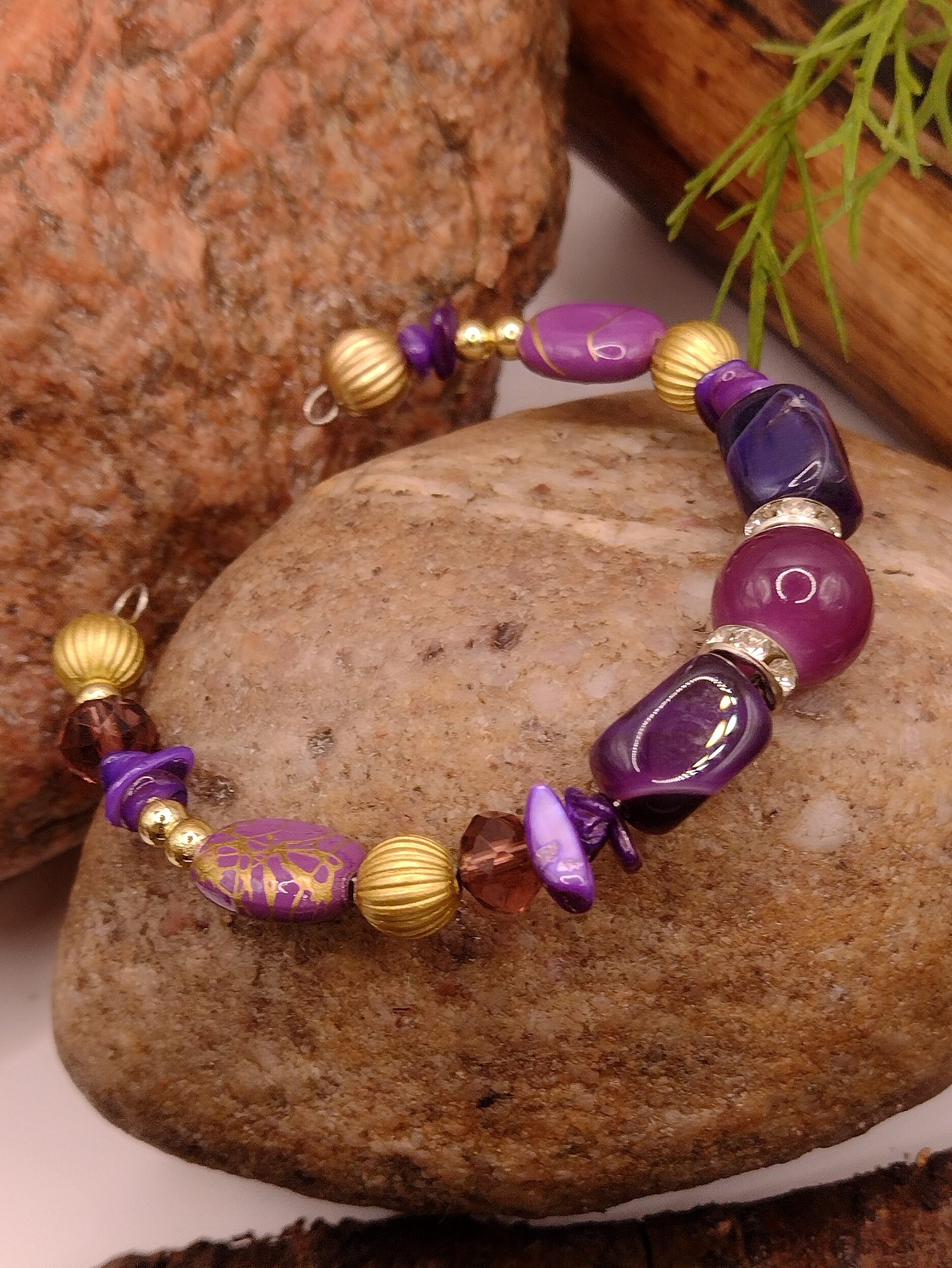 Fioletowa bransoletka na drucie pamięciowym z centralnym koralikiem, złotymi przekładkami z kryształkami oraz muszlowymi kamyczkami, biżuteria handmade
