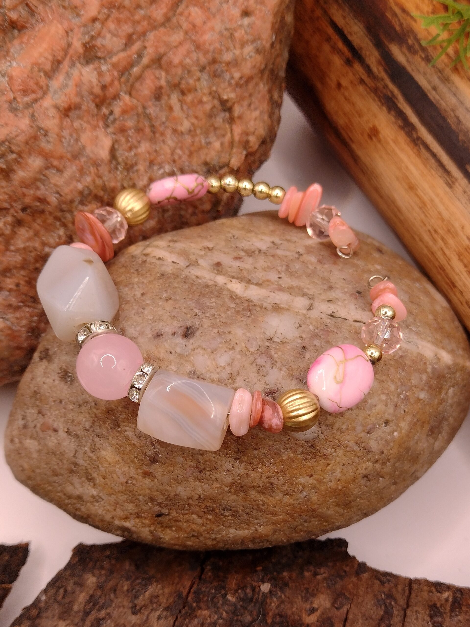 Bransoletka na drucie pamięciowym z jasnoróżowymi i delikatnie ciemniejszymi koralikami, z metalowymi kuleczkami i złotymi przekładkami z kryształkami.