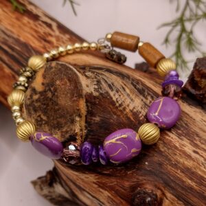 Bransoletka na drucie pamięciowym z fioletowymi koralikami, fioletowymi muszlowymi koralikami, fasetowanymi szklanymi koralikami w odcieniu brązu, z metalowymi złotymi kuleczkami i złotymi przekładkami.
