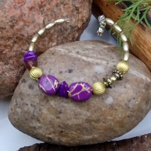 Bransoletka na drucie pamięciowym z fioletowymi koralikami, fioletowymi muszlowymi koralikami, fasetowanymi szklanymi koralikami w odcieniu brązu, z metalowymi złotymi kuleczkami i złotymi przekładkami.