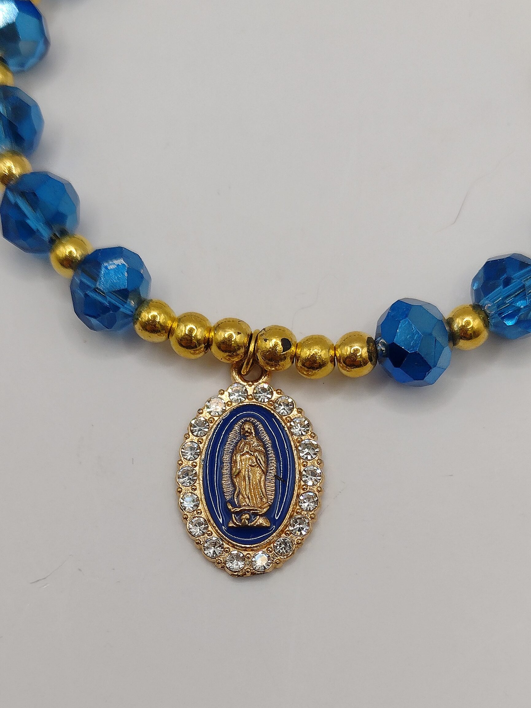 Ręcznie wykonana bransoletka-różaniec z szafirowych fasetowanych koralików i złotych akcentów, z ozdobnym krzyżykiem oraz medalikiem Matki Boskiej na regulowanym zapięciu.