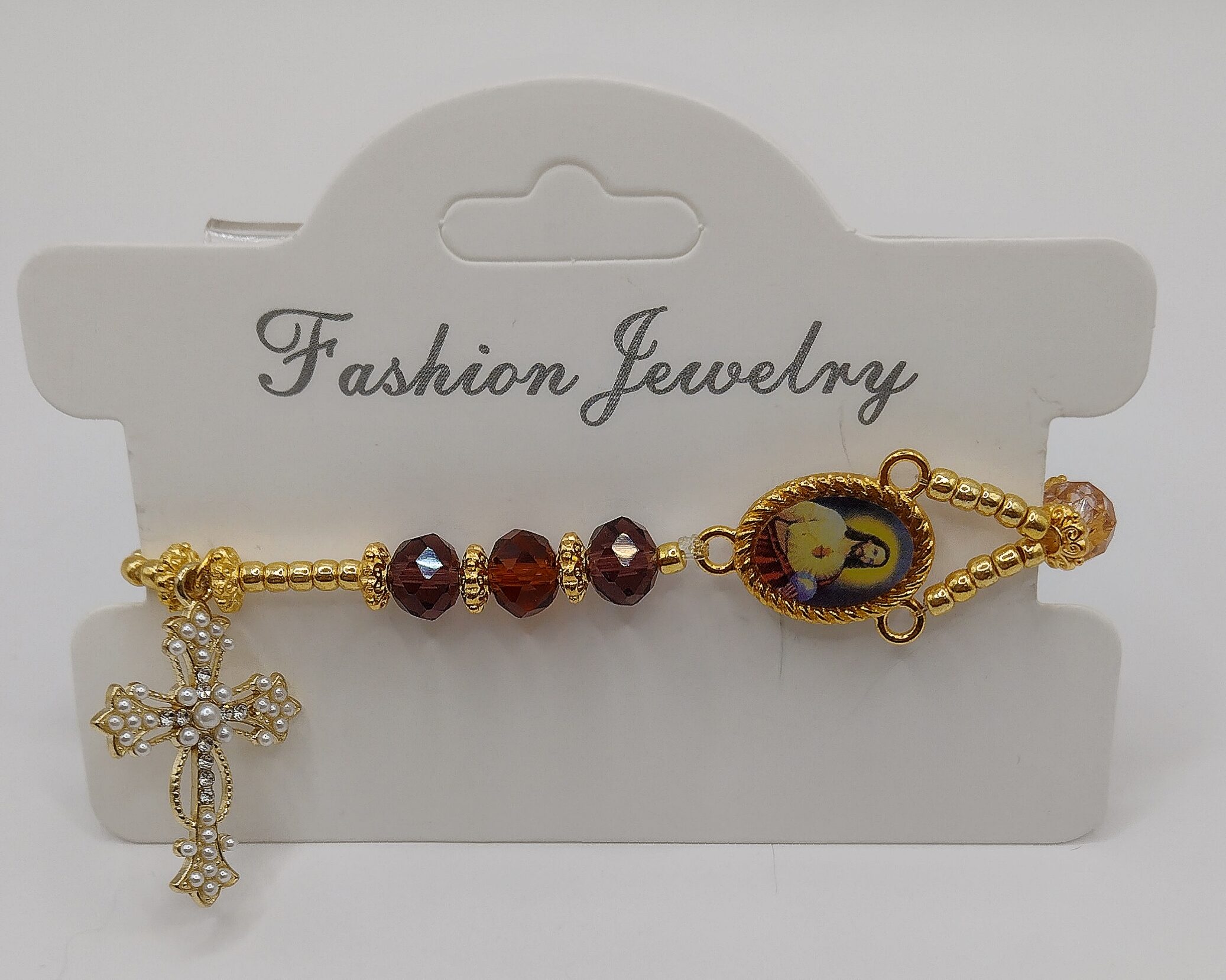 Bransoletka‑różaniec z fasetowanych koralików w kremowo‑brązowych odcieniach, z medalikiem Jezusa i ozdobnym krzyżykiem.