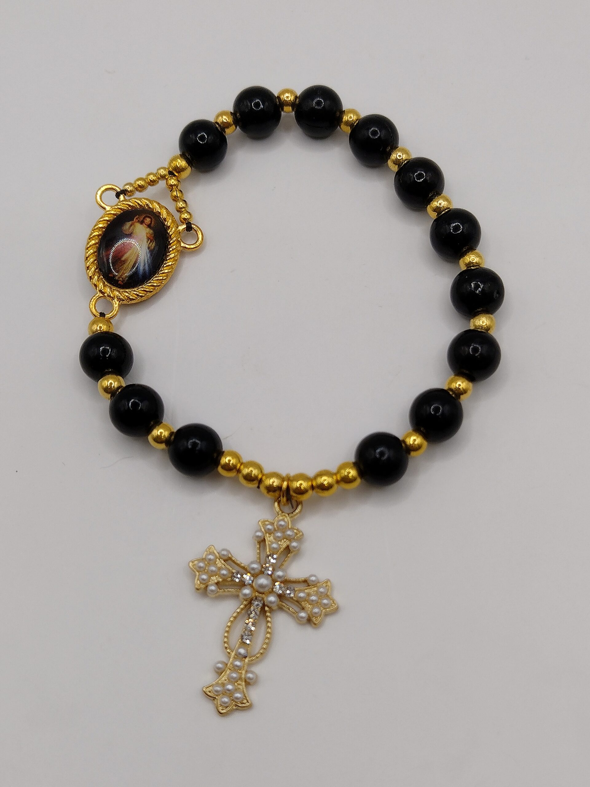 Bransoletka‑różaniec „Modlitwa Ochrony” z czarnych perełek, z medalikiem Jezusa i ozdobnym krzyżykiem.