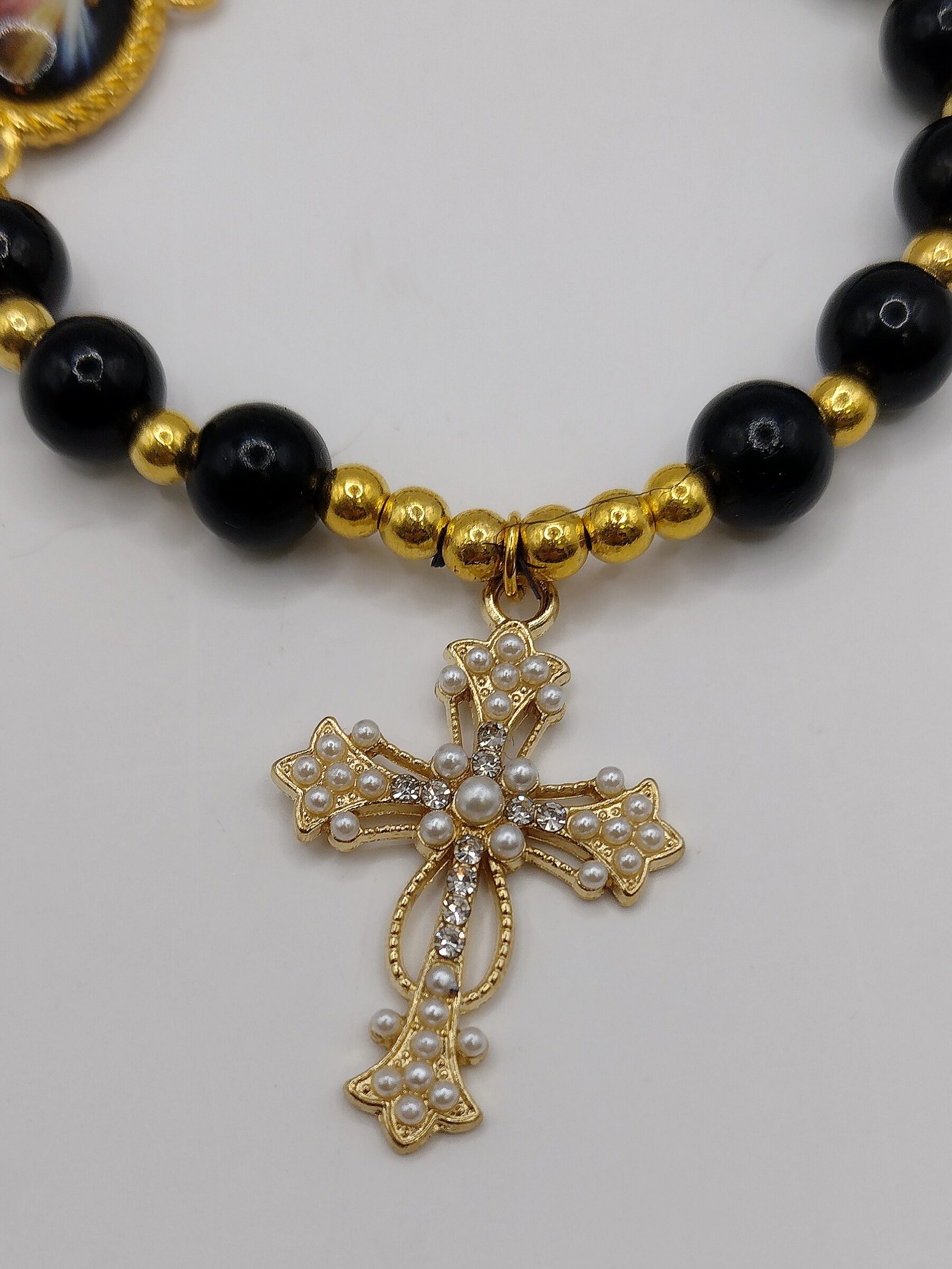 Bransoletka‑różaniec „Modlitwa Ochrony” z czarnych perełek, z medalikiem Jezusa i ozdobnym krzyżykiem.