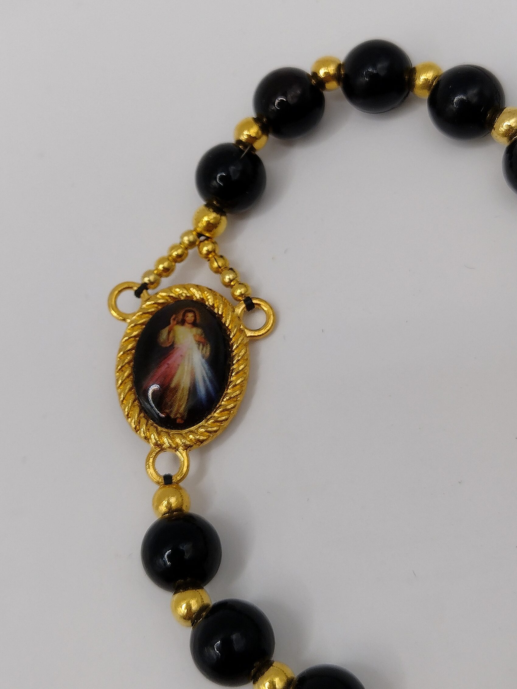 Bransoletka‑różaniec „Modlitwa Ochrony” z czarnych perełek, z medalikiem Jezusa i ozdobnym krzyżykiem.
