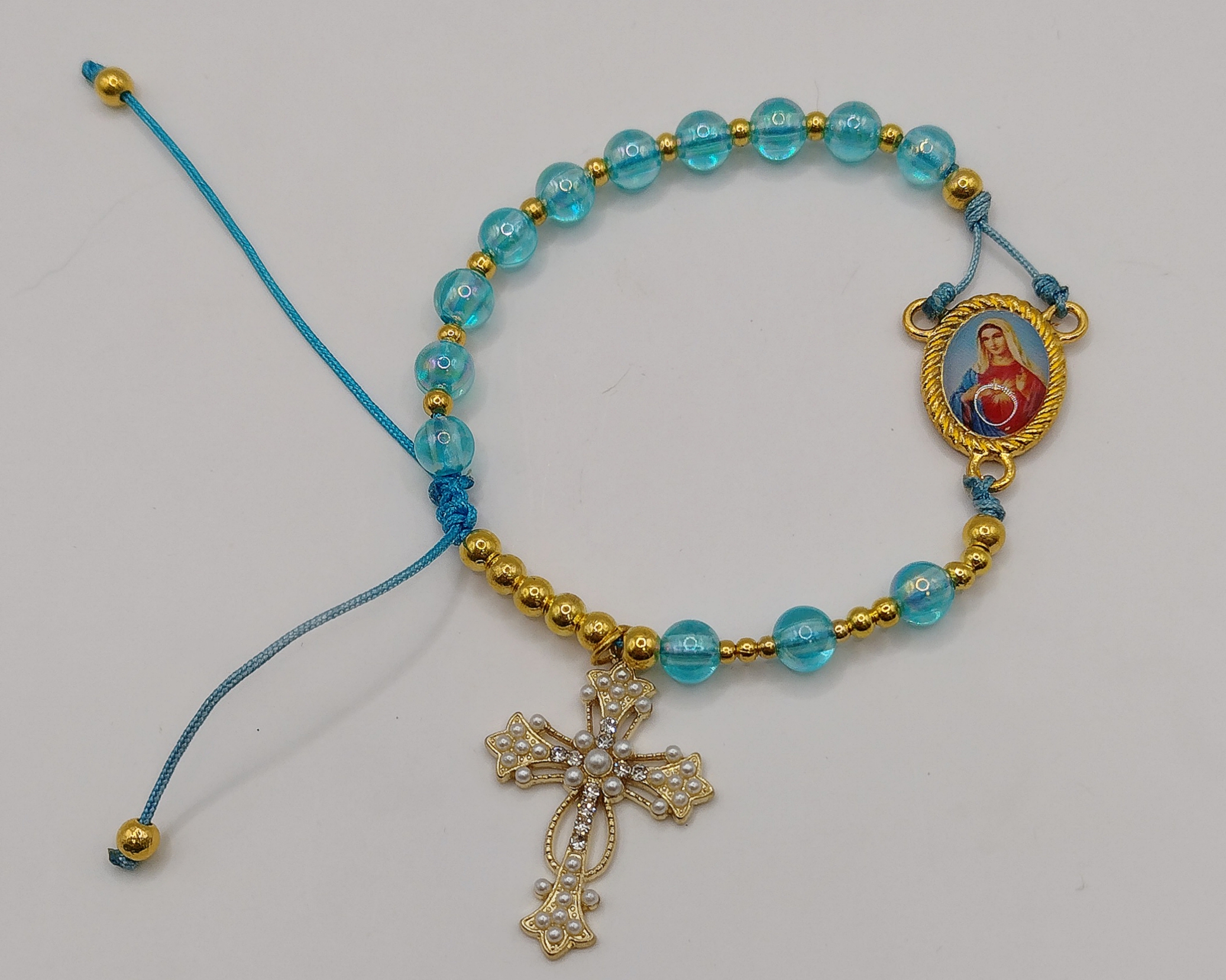 Ręcznie wykonana bransoletka religijna z turkusowych koralików i złotych przekładek, z ozdobnym krzyżykiem oraz medalikiem Matki Boskiej na regulowanym sznurku.