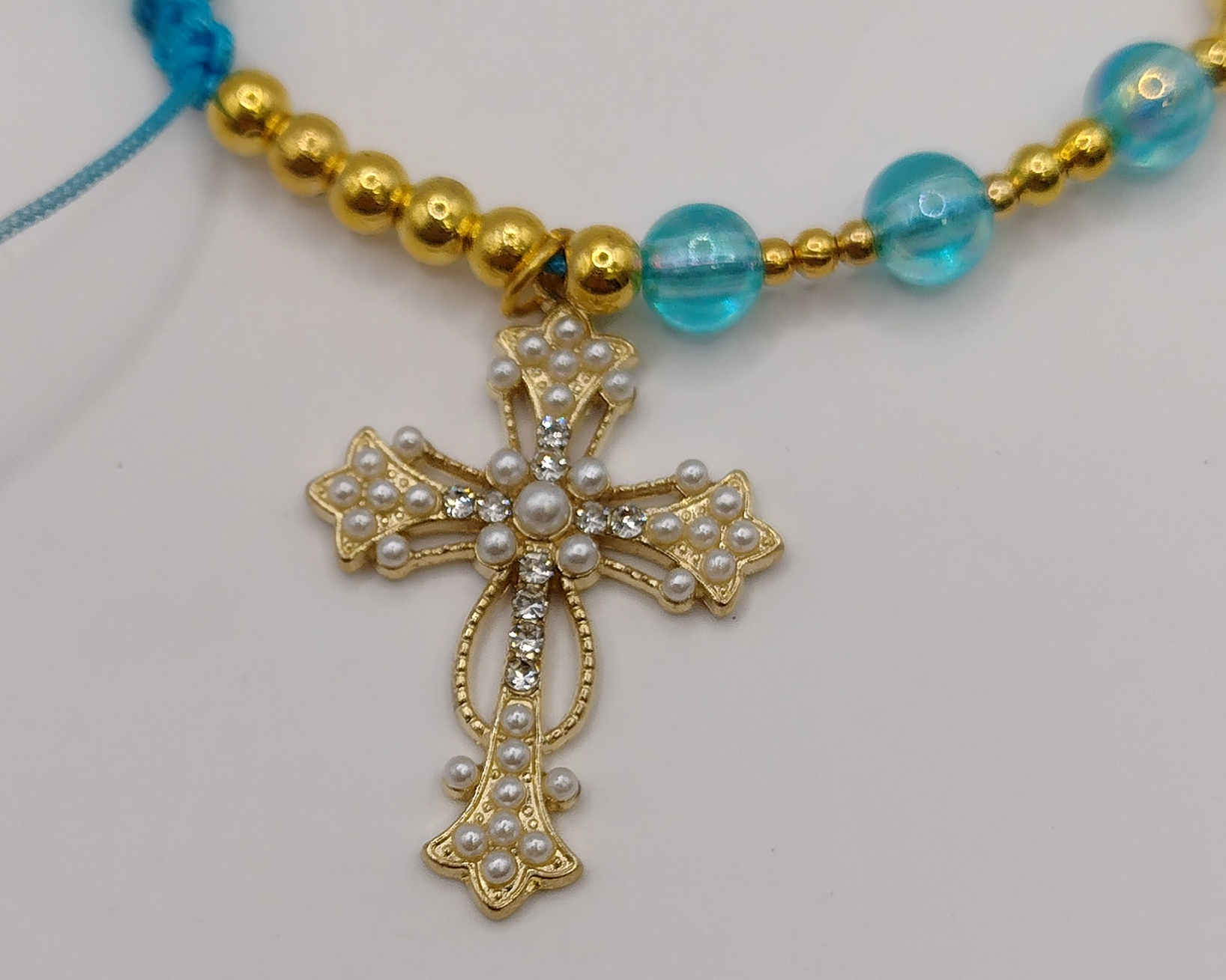 Ręcznie wykonana bransoletka religijna z turkusowych koralików i złotych przekładek, z ozdobnym krzyżykiem oraz medalikiem Matki Boskiej na regulowanym sznurku.