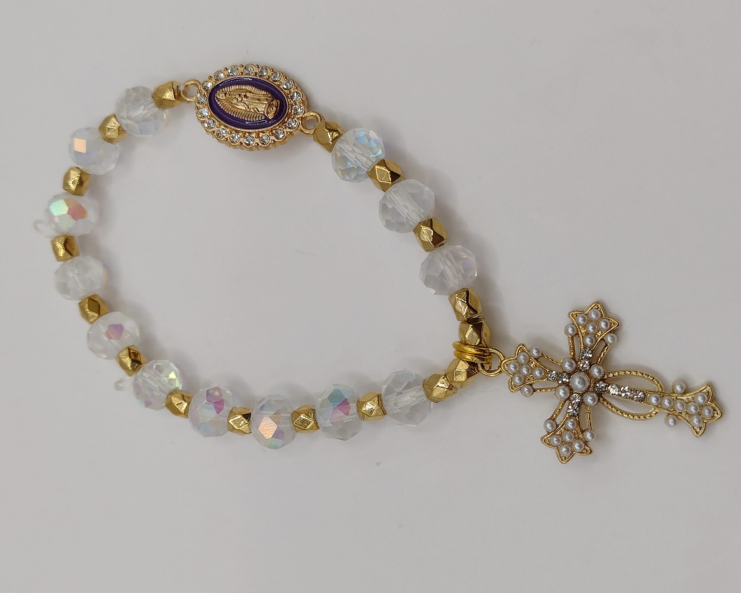 Bransoletka‑różaniec z białych fasetowanych koralików na elastycznej gumce, z ozdobnym krzyżykiem i medalikiem Matki Boskiej.