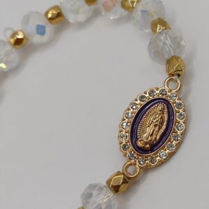 Bransoletka‑różaniec z białych fasetowanych koralików na elastycznej gumce, z ozdobnym krzyżykiem i medalikiem Matki Boskiej.