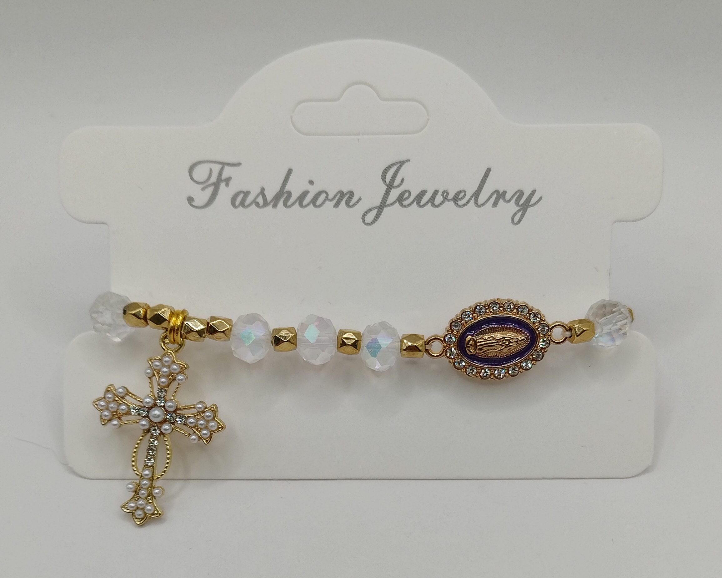 Bransoletka‑różaniec z białych fasetowanych koralików na elastycznej gumce, z ozdobnym krzyżykiem i medalikiem Matki Boskiej.