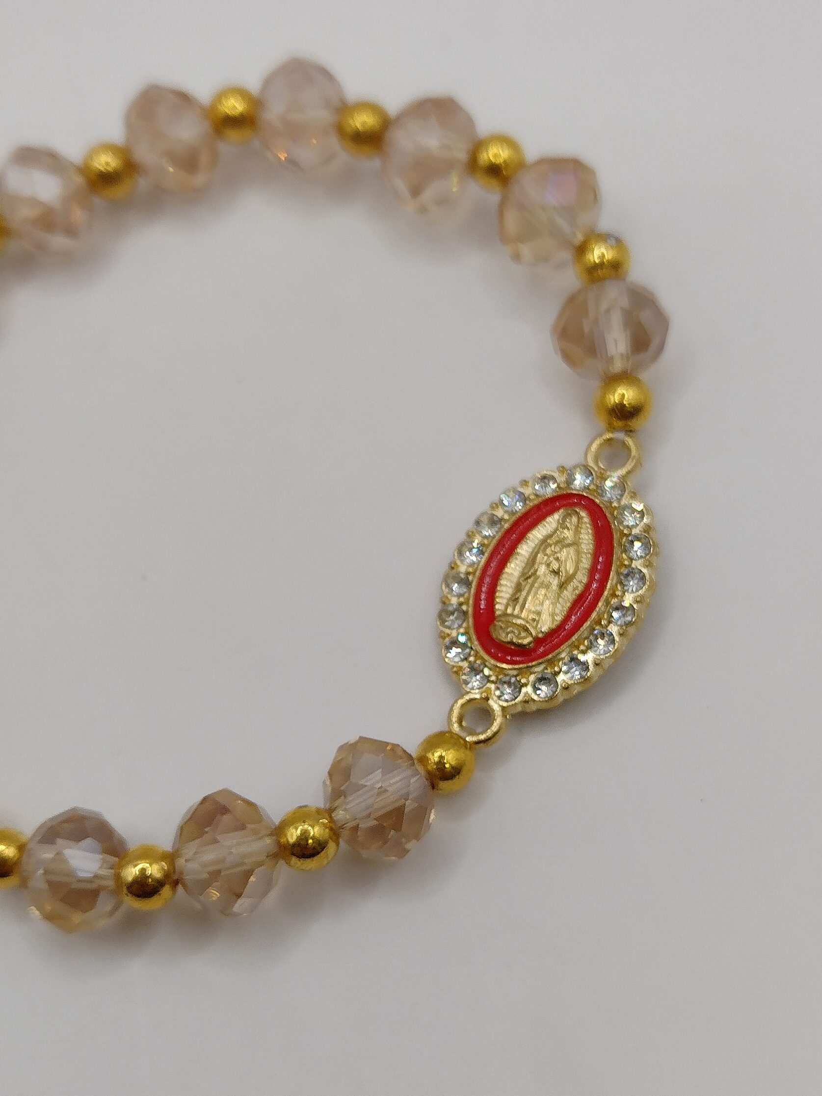 Bransoletka‑różaniec z białych fasetowanych koralików na gumce, z ozdobnym krzyżykiem i medalikiem Matki Boskiej